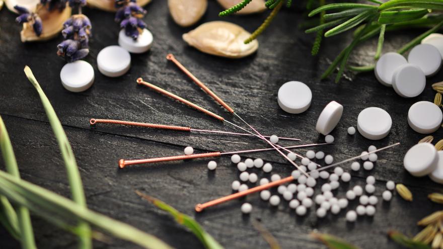 Akupunkturnadeln, Tabletten und Pflanzen auf einer Schiefertafel